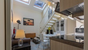 En kompakt opholdsstue med et tekøkken, spiseplads og en trappe til en etage ovenover.