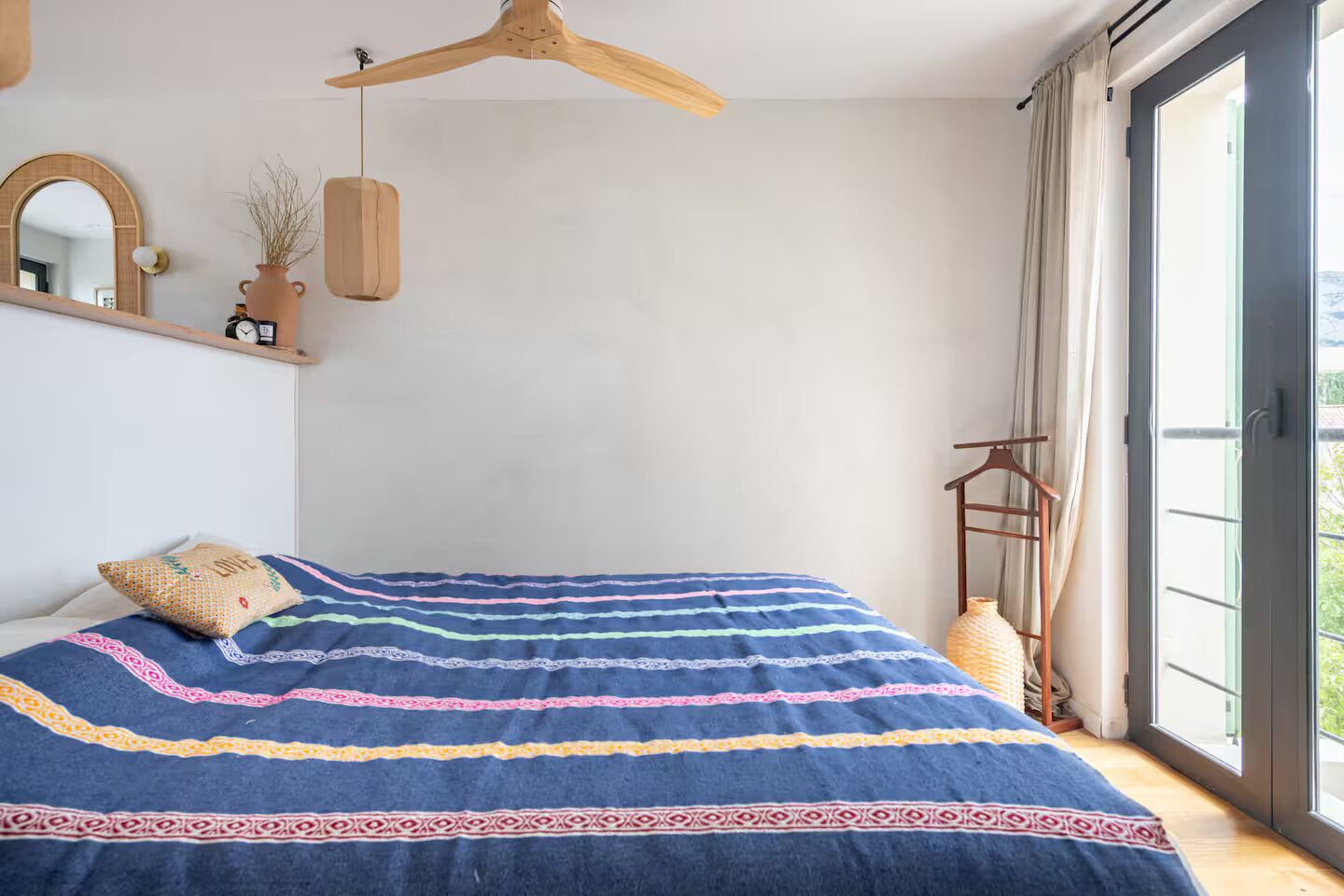 Un dormitorio con una cama grande, un ventilador de techo de madera, una planta colgante y vistas por la ventana.