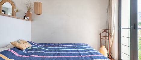 Un dormitorio con una cama grande, un ventilador de techo de madera, una planta colgante y vistas por la ventana.