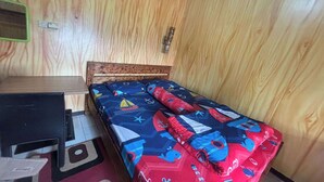 Pieni huone, jossa on yksi sänky, puinen pääty ja työpöytä sekä tuoli.