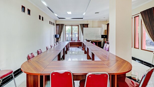 Une salle de conférence avec une longue table en bois, des chaises rouges et un tableau blanc.