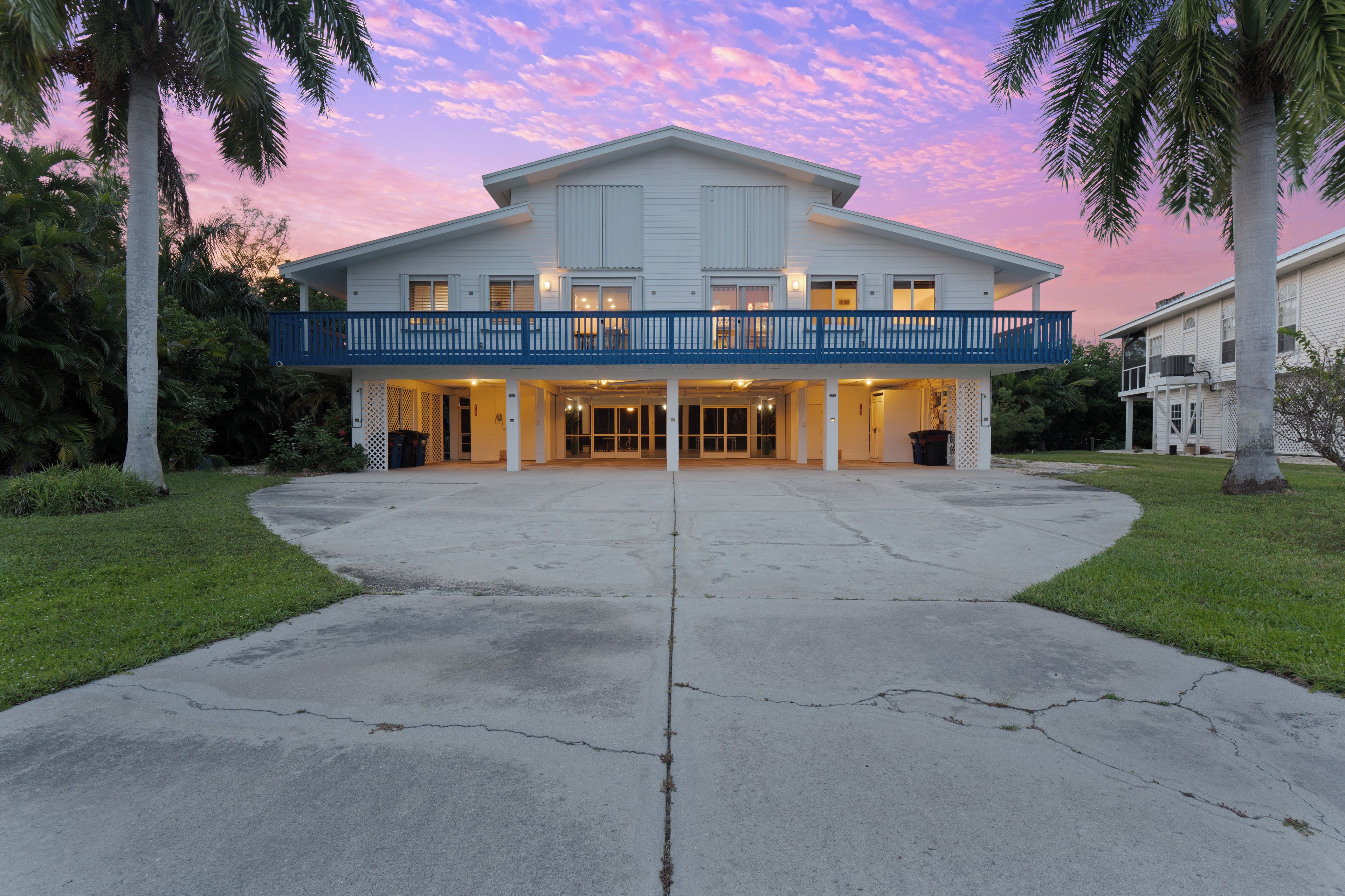 A two-story house with a balcony, a driveway, and palm trees.