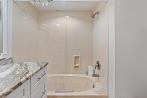 A bathroom with a bathtub, a shower, and a marble countertop.