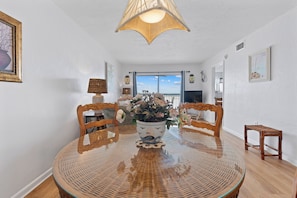 A dining area with a round glass table, wicker chairs, a potted plant, and a view to the outside.