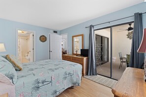 Un dormitori amb llit, commode, televisió i una porta corredissa de vidre que dona a un balcó.