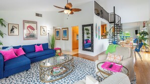 Ein geräumiges Wohnzimmer mit einem blauen Sofa, einem Glastisch und einer Treppe, die zu einer oberen Ebene führt.