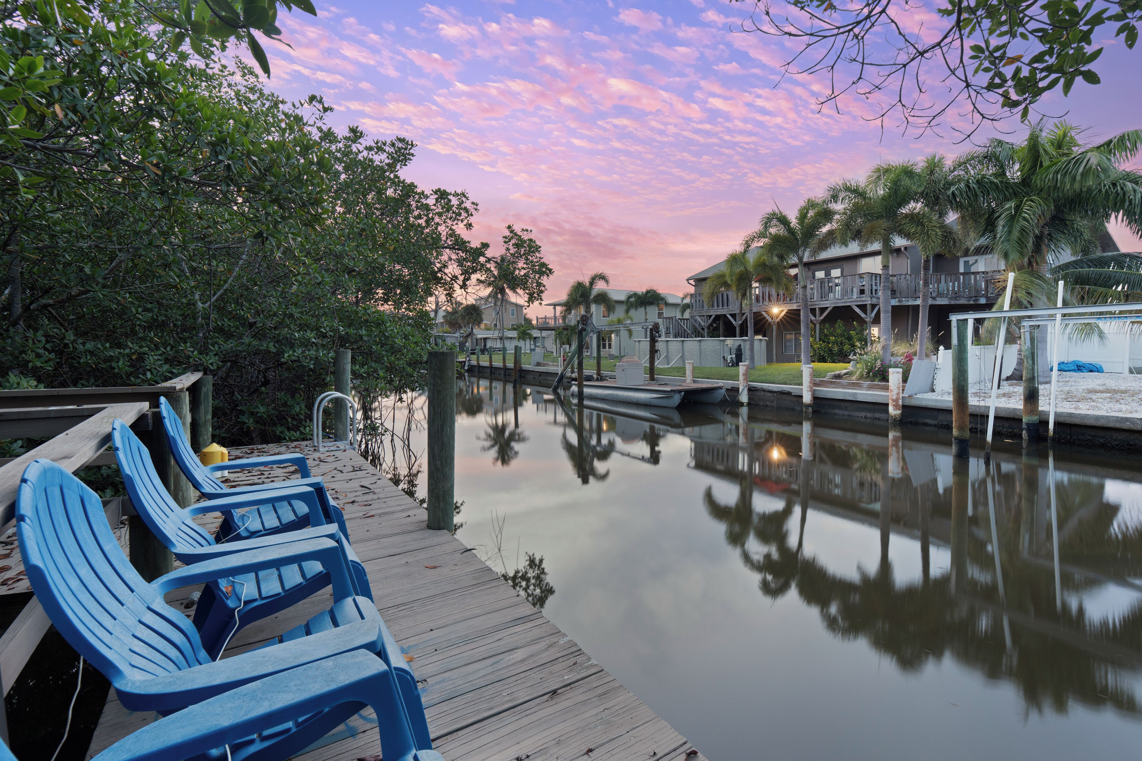 A waterfront property with a wooden dock, lounge chairs, and a calm water body reflecting the surroundings.