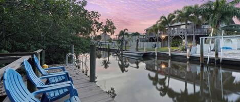 A waterfront property with a wooden dock, lounge chairs, and a calm water body reflecting the surroundings.