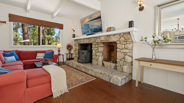 A living room with a stone fireplace, red leather sofa, and a large window with blinds. - Walk to the lake Gorgeous lake house (Big Bear Lake)