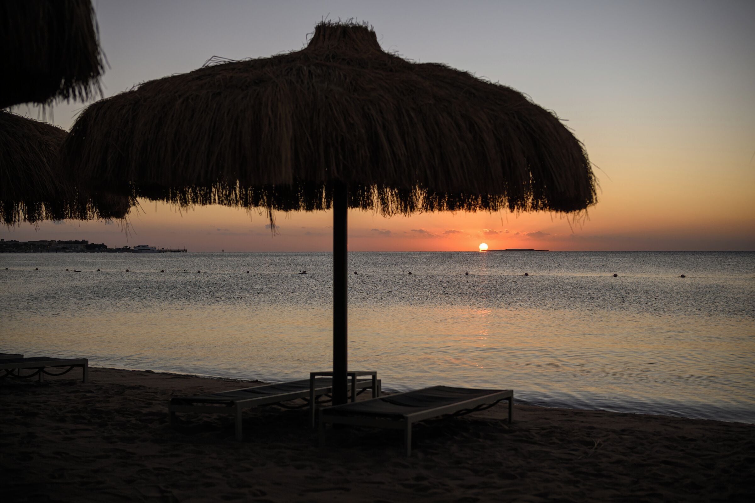 Una sombrilla de playa, sillas de descanso y un atardecer sobre el océano.