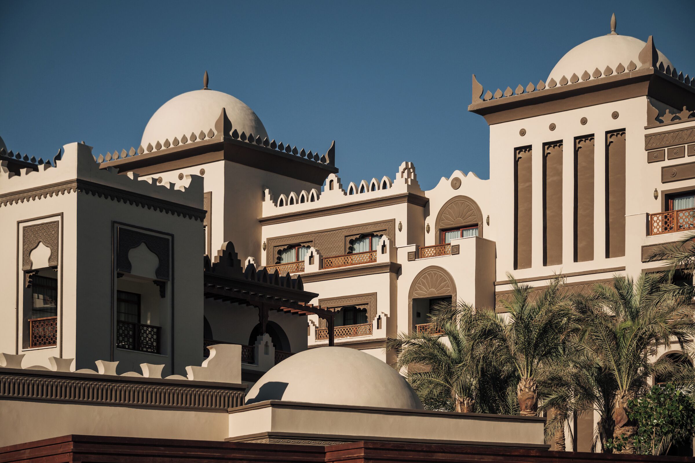 A multi-story building with domed structures, balconies, and palm trees.