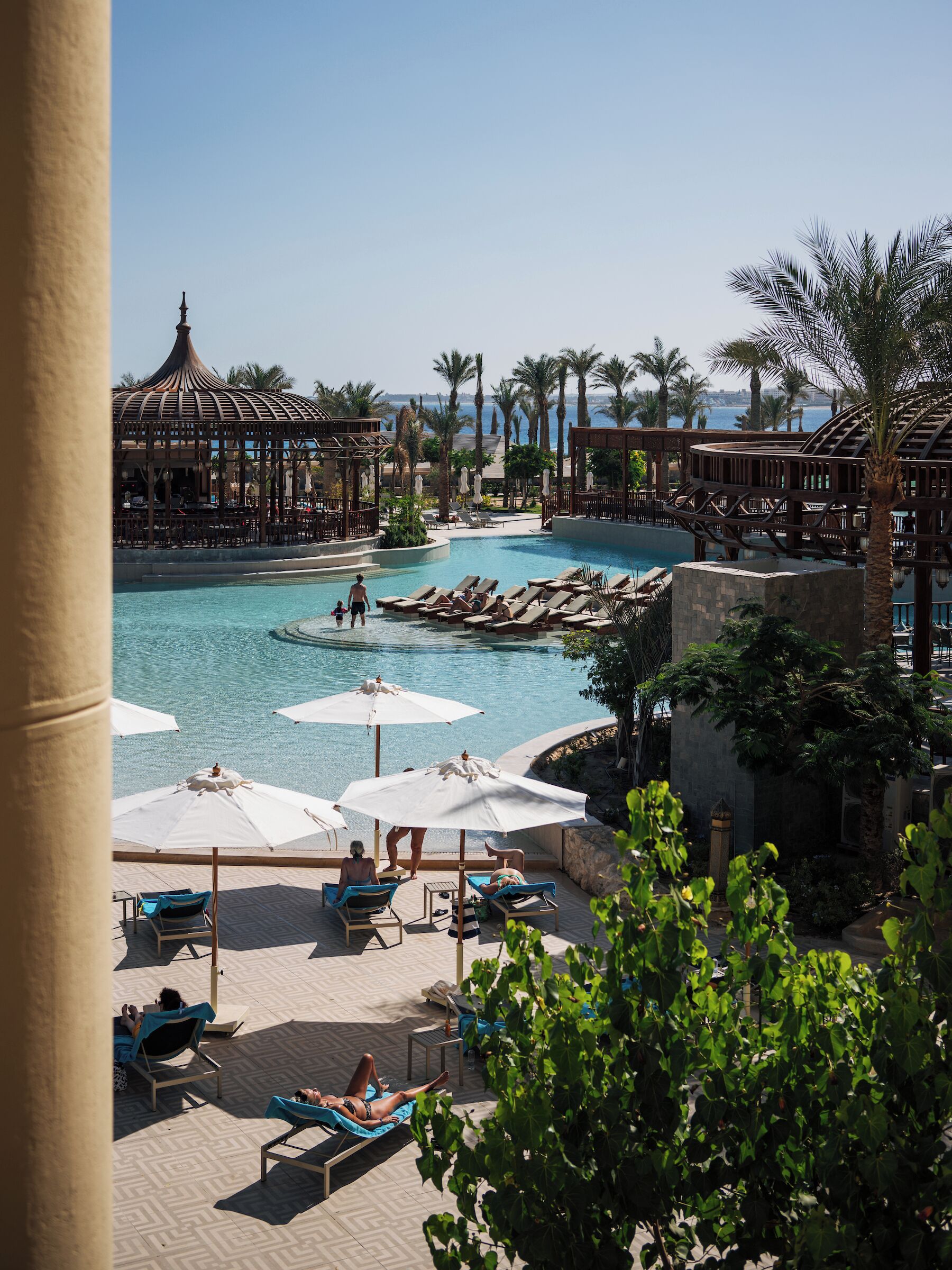 Zona de piscina en un resort con sillones, sombrillas y vista al mar.