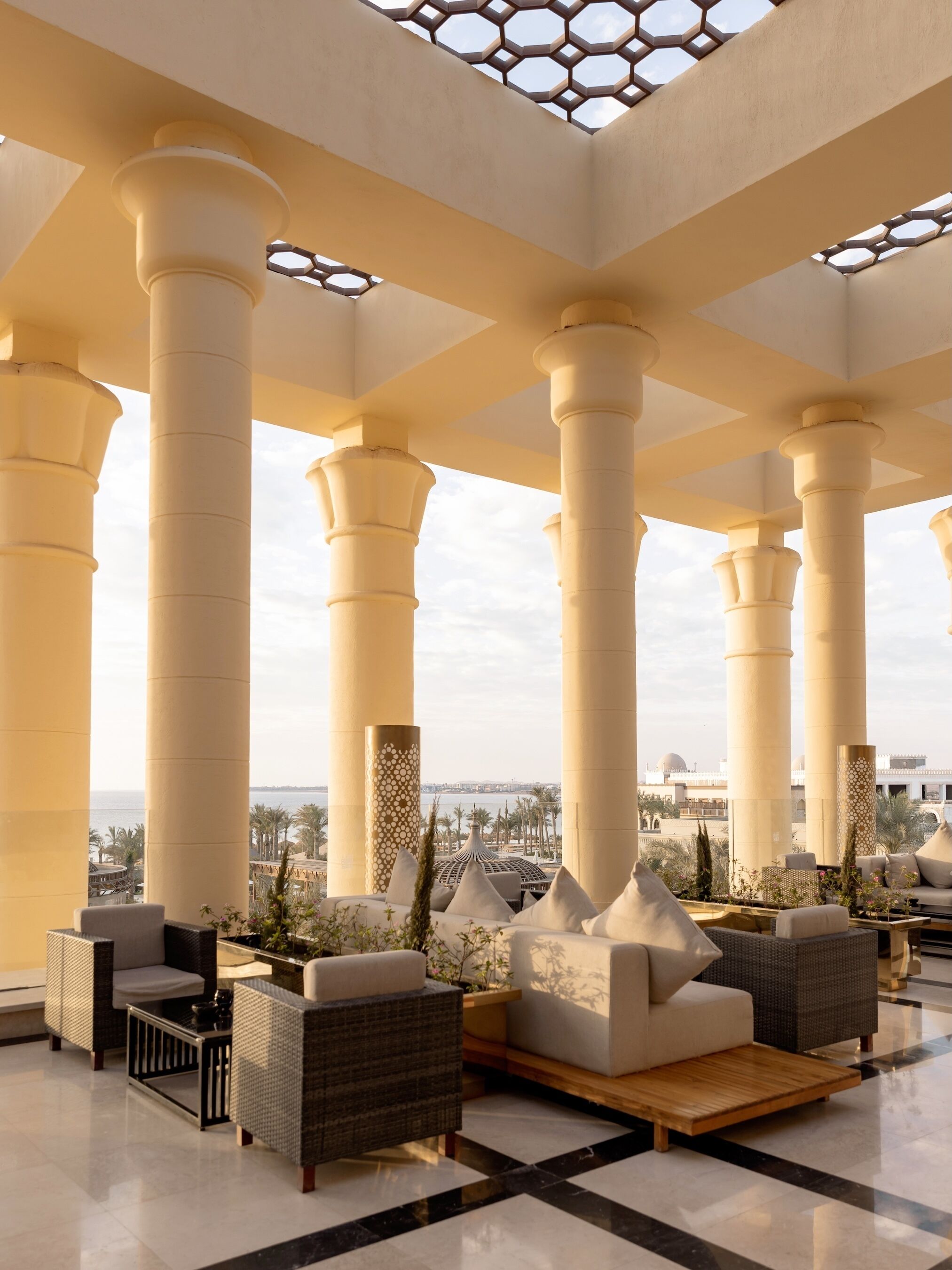 Eine Lobby mit großen Säulen, einer Sitzecke mit Sofas und Sesseln und Blick aufs Meer.
