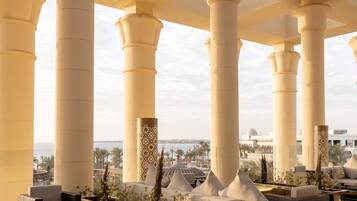 Eine Lobby mit großen Säulen, einer Sitzecke mit Sofas und Sesseln und Blick aufs Meer.