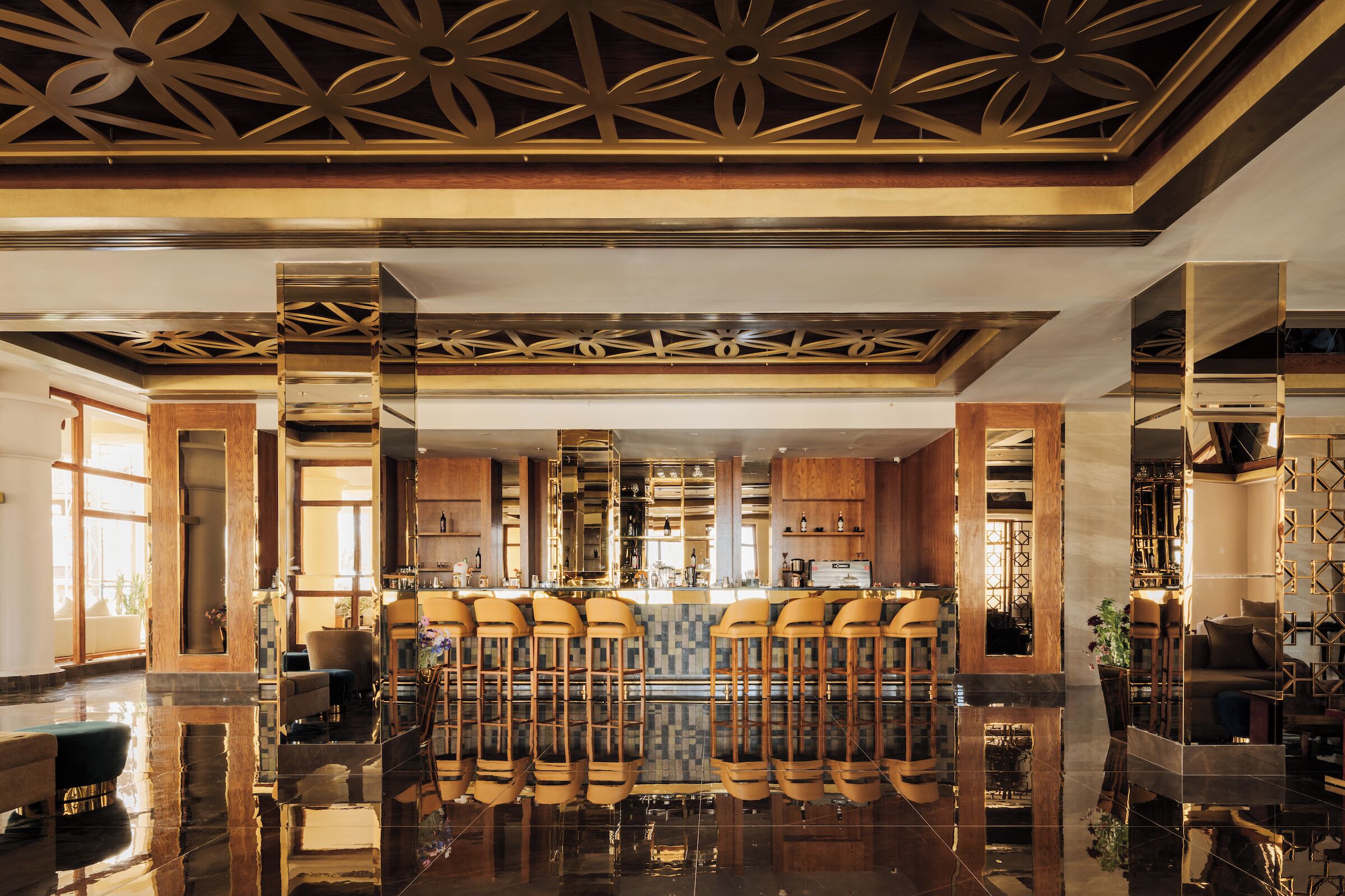 A bar area with high stools, a polished floor, and a decorative ceiling.