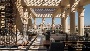 A luxurious outdoor lounge area with seating, a patterned ceiling, and a view of a grand building in the background. - Al Kasr Sahl Hasheesh-Ultra All-Inclusive (Sahl Hasheeh)