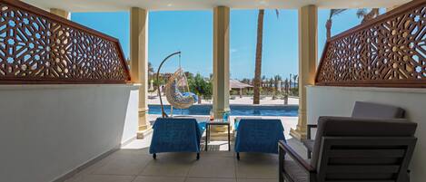 A balcony with two chairs, a table, and a view of a swimming pool.