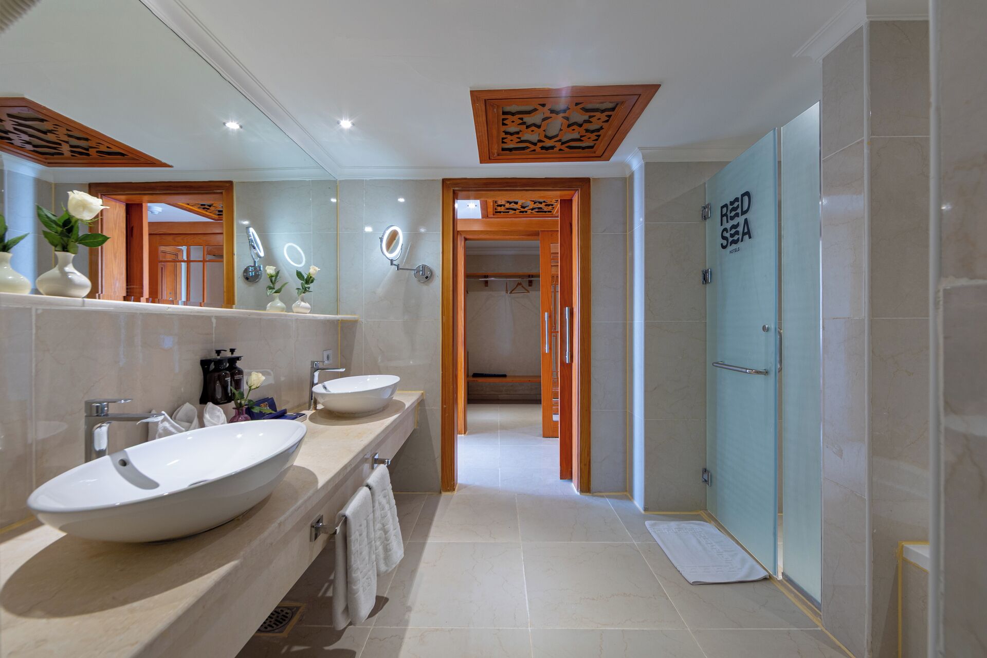 A modern bathroom with two large sinks, a mirror with built-in lights, a shower area, and a visible door labeled 'RED SEA HOTEL'.