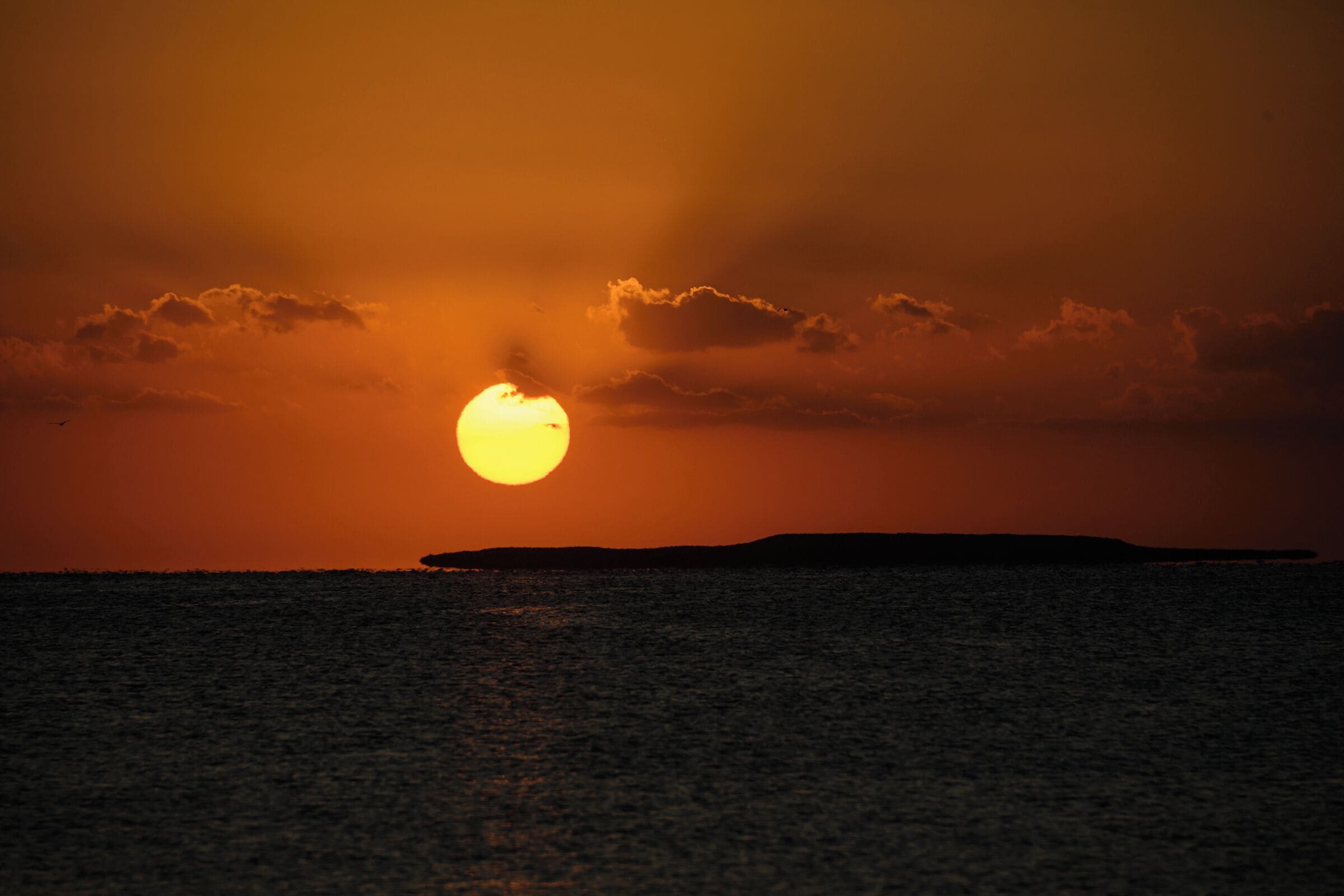 A sunset over a body of water with a silhouette of a landmass in the distance.