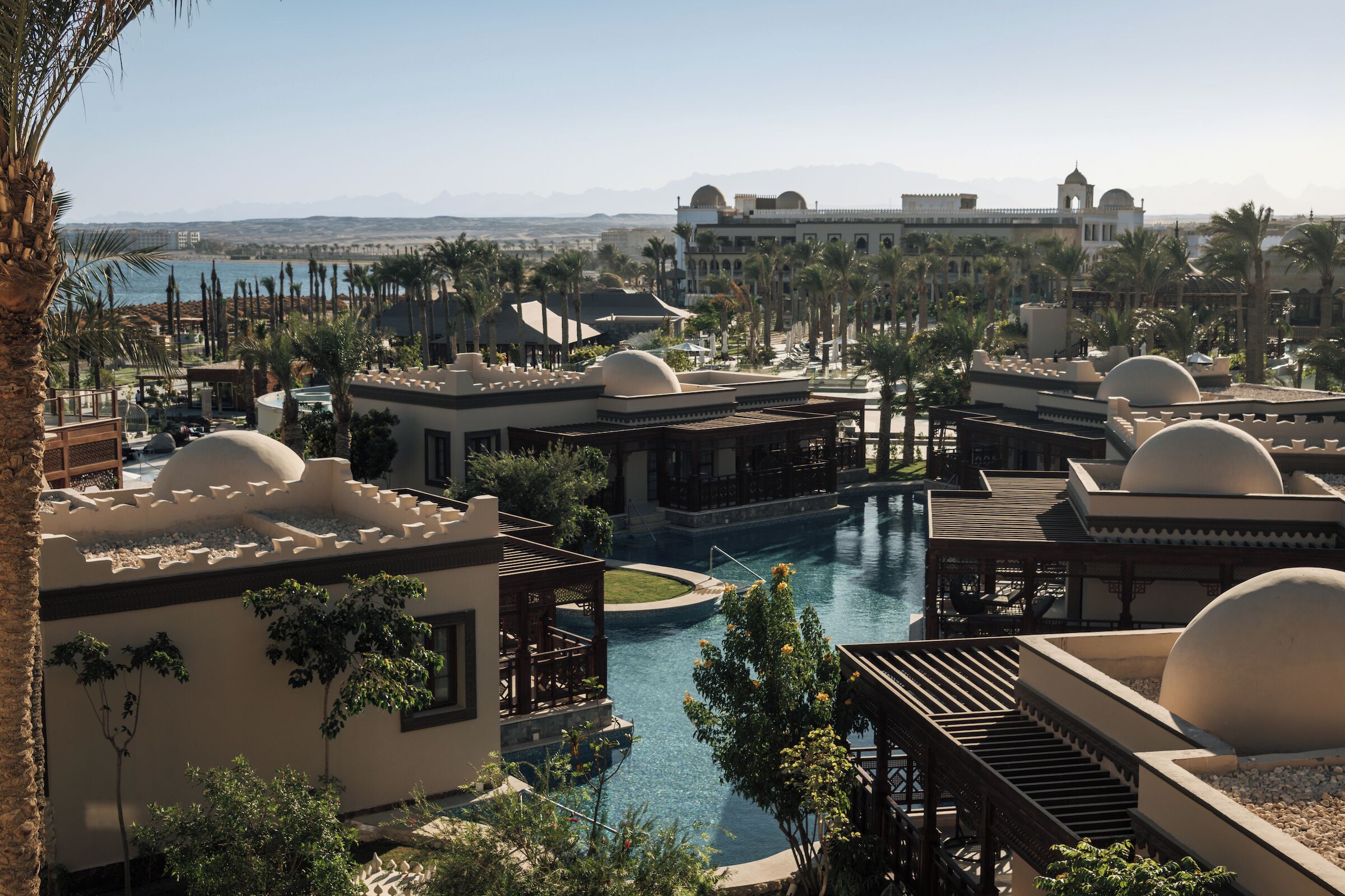 A resort with a swimming pool, palm trees, and a view of the mountains.