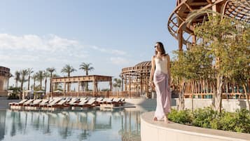 A poolside area with lounge chairs, a wooden pergola, and a clear sky.