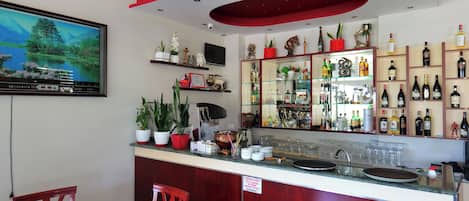 A bar area with a counter, shelves of bottles, and a television mounted on the wall.