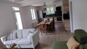 A modern living room with a white sofa, a green sofa, and a dining area with wooden chairs and a table. - Quiet house in a large park. Close to the coast and shops! (Lamballe-Armor)