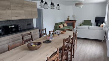 Une cuisine moderne avec des meubles en bois, une table à manger avec des chaises, un four à micro-ondes et des luminaires suspendus.