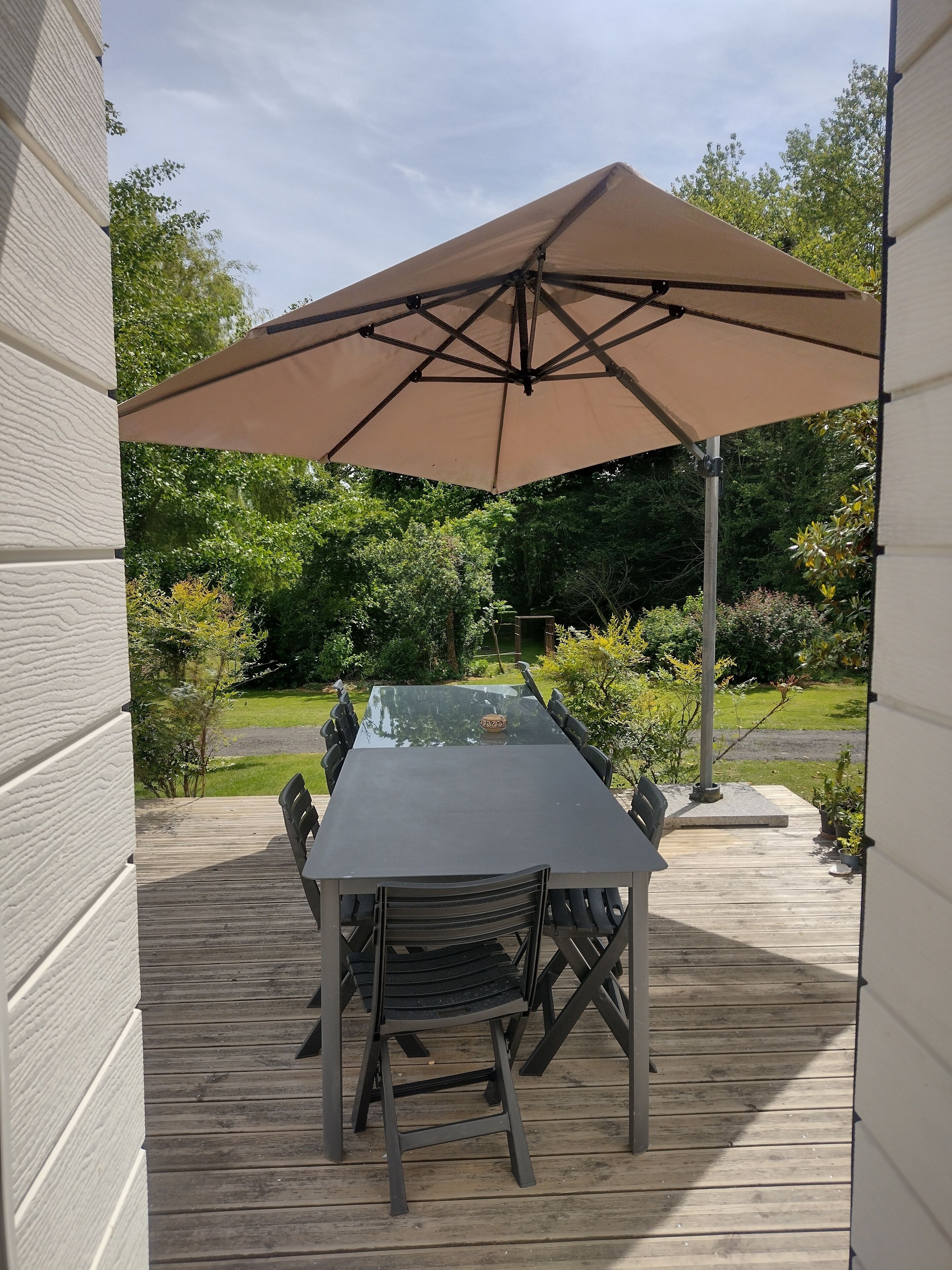 Eine Außenpatio mit Tisch und Stühlen, einem großen Sonnenschirm und Blick auf einen Garten.