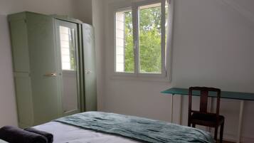 Une chambre à coucher avec un lit, une armoire verte, un bureau avec une chaise et une fenêtre donnant sur des arbres.
