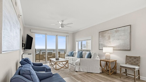 A spacious living room with a large window, a ceiling fan, a flat-screen TV, a sofa set, a coffee table, and a side table with a lamp. - Enclave 607 (Orange Beach)