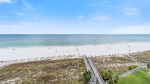 A beach with a wooden boardwalk leading to the shore, a grassy area, and a clear view of the ocean. - Enclave 607 (Orange Beach)