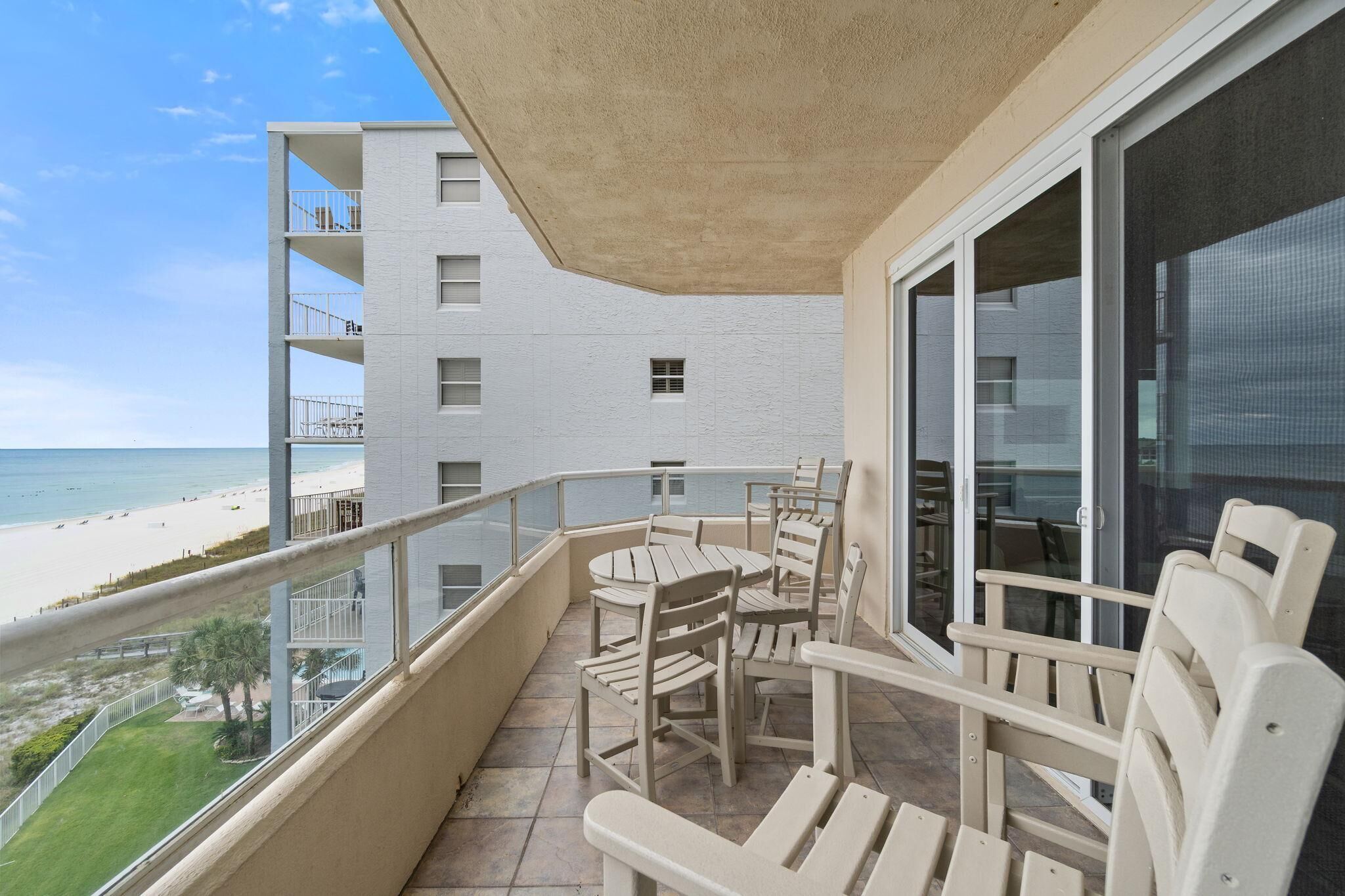 A balcony with a table and chairs, overlooking a beach and a white building.