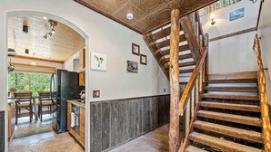 Una cocina amplia con armarios de madera y una isla grande, una escalera de madera rústica y un comedor con sillas de madera.