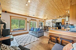 A spacious living room with a large gray sofa, a wooden ceiling, and a kitchen area with modern appliances. - Rustic 5BR Retreat | Hot Tub, Near Park City (Coalville)