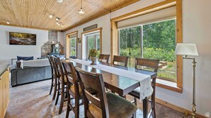 Un comedor espacioso con una larga mesa, sillas de madera y vistas a un jardín exuberante a través de amplios ventanales.