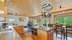 Una cocina amplia con armarios de madera, encimera de granito y una isla grande. Hay un comedor con sillas y mesa de madera, y un rincón de estar acogedor con sofá y chimenea.