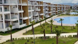 Un moderno complejo de apartamentos con varios balcones, una piscina central y jardines bien cuidados.