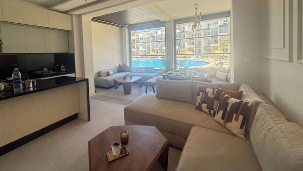 Una sala de estar moderna con sofá, mesa de centro y vistas a una piscina y edificios.