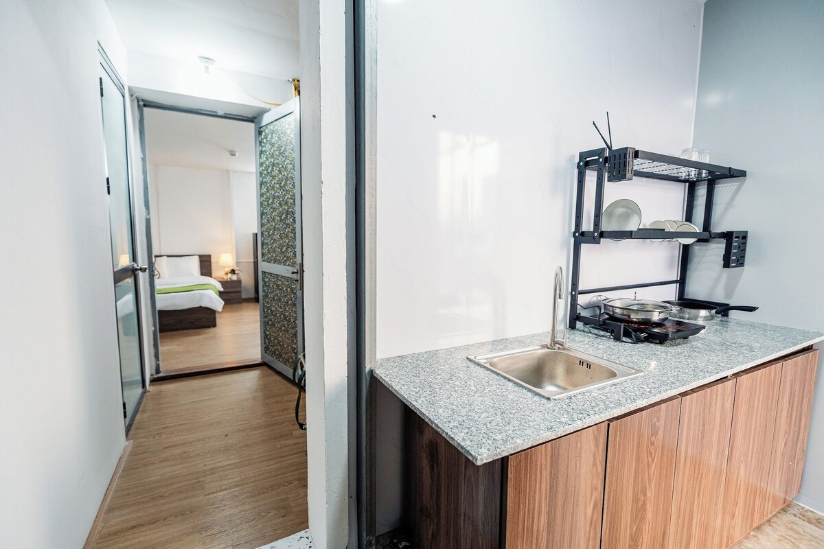 A compact kitchen with a granite countertop, a built-in sink, and a black metal shelf unit.