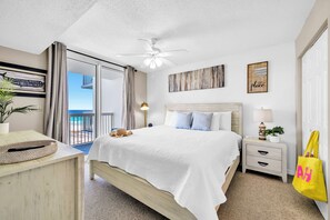 A bedroom with a bed, a nightstand, a ceiling fan, a view of the outdoors, and a yellow bag. - ☀️ Pelican Beach 918 - Après Beach 🌊 (Destin)