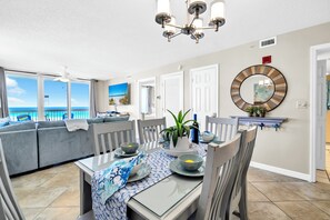 A dining area with a table set for four, a sofa, a ceiling fan, and a view of the ocean. - ☀️ Pelican Beach 918 - Après Beach 🌊 (Destin)