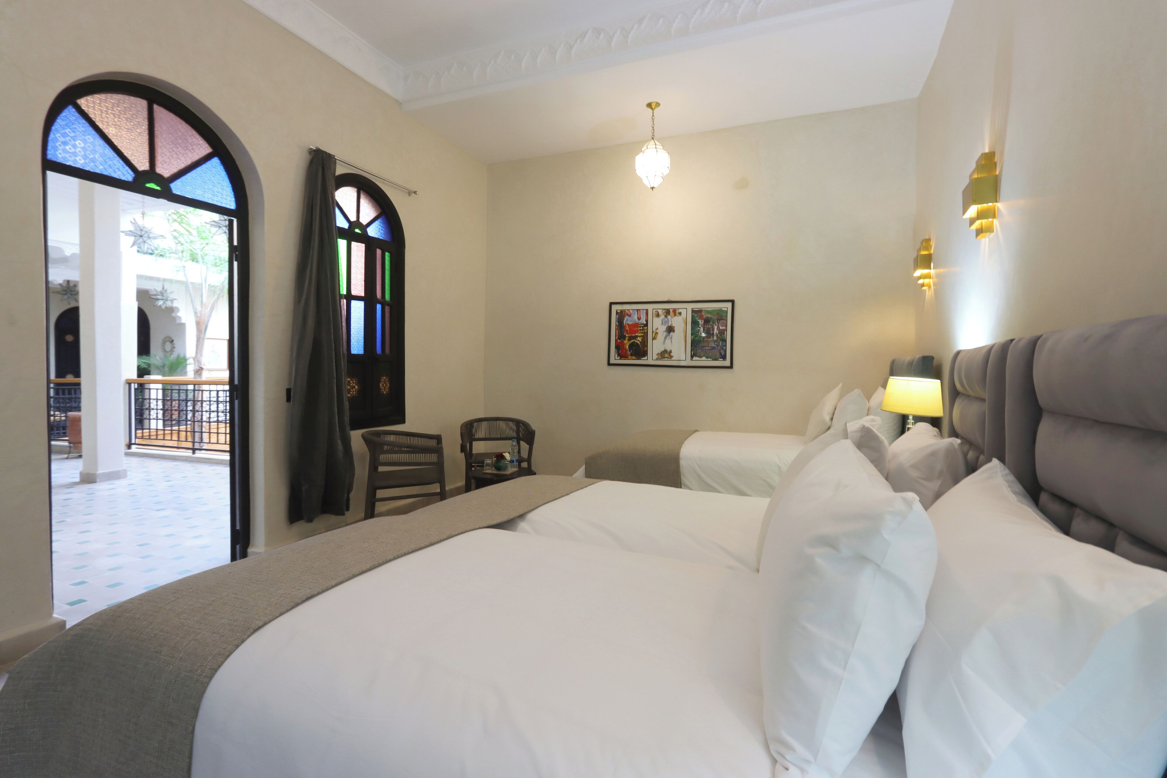 Une chambre d’hôtel avec un grand lit, deux tables de chevet, une chaise, une fenêtre donnant sur un beau paysage et un lustre.