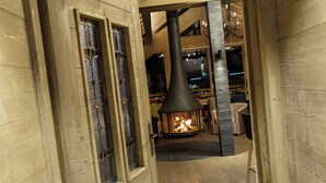 A wooden interior with a fireplace, wooden beams, and a stone column. - Luxury Catered Ski Chalet Iona in Meribel, France LMRB-9 (Meribel)