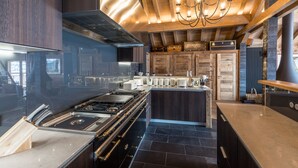 A modern kitchen with a central island, stainless steel appliances, and wooden beams. - Luxury Catered Ski Chalet Iona in Meribel, France LMRB-9 (Meribel)