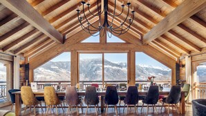A dining area with a wooden ceiling and large windows overlooking a snowy mountain range. - Luxury Catered Ski Chalet Iona in Meribel, France LMRB-9 (Meribel)