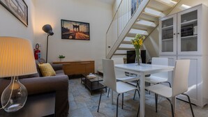Uma sala de estar moderna com sofá, mesa de centro e mesa de jantar. Há uma escada que leva a um andar superior, e um quadro na parede.