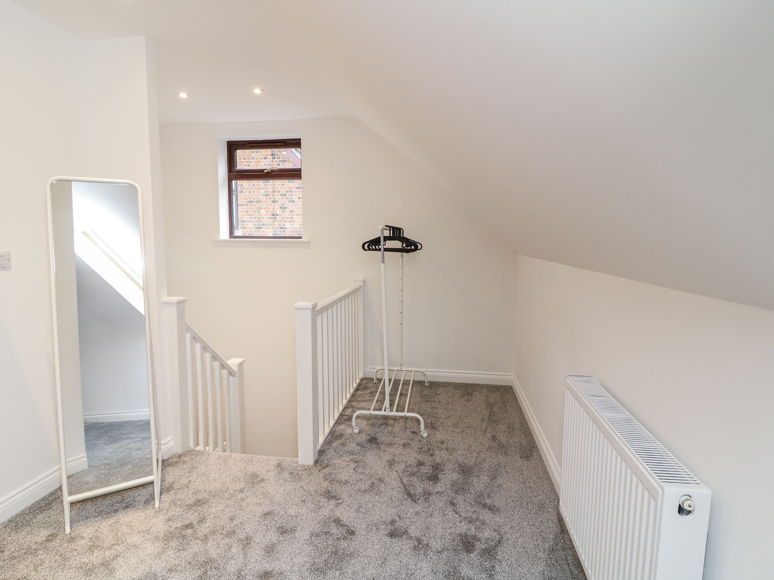 A clean, well-lit attic room with a sloped ceiling, a small window, a radiator, and a metal ladder.