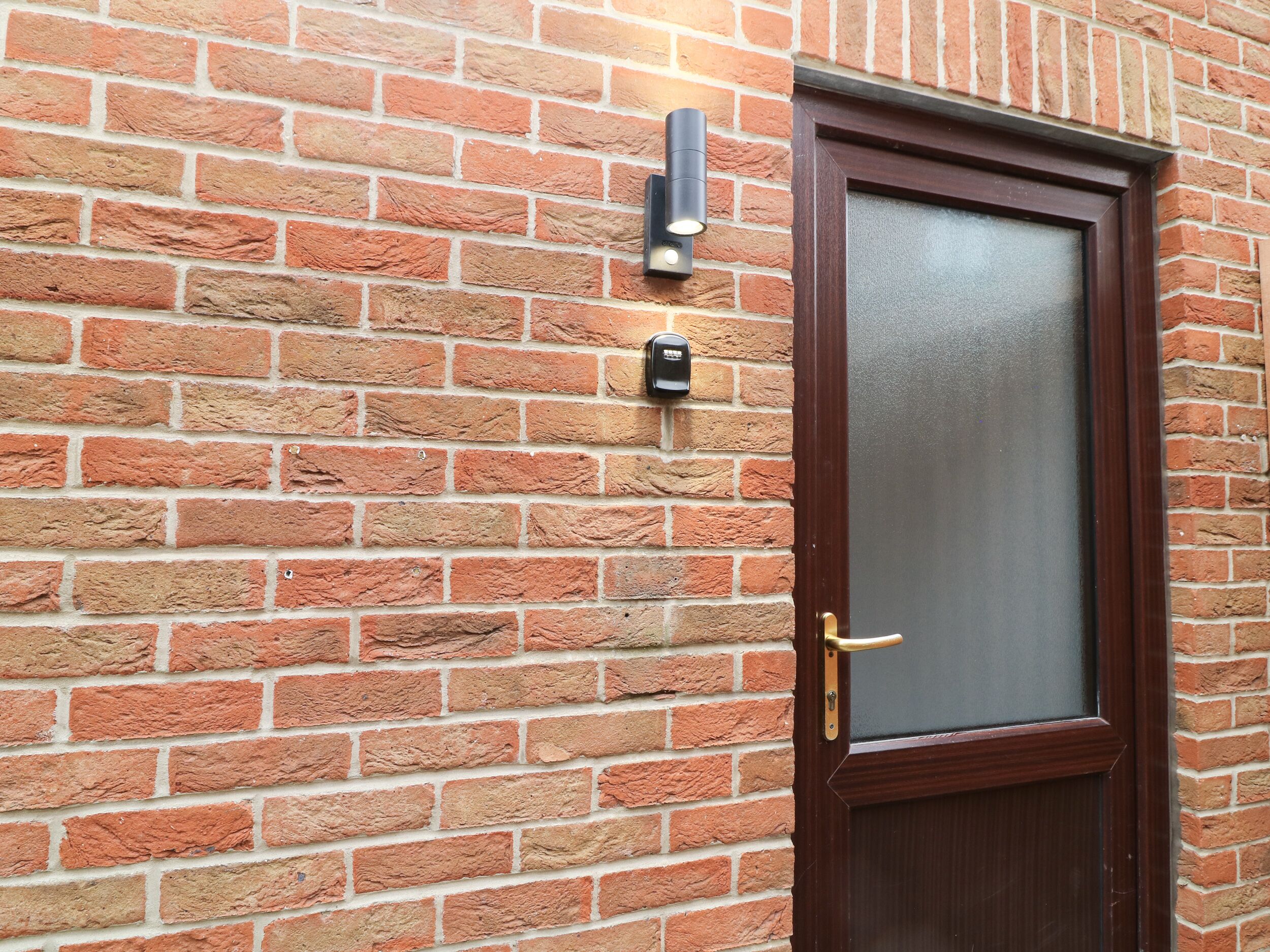 A brick wall with a door and a security device.