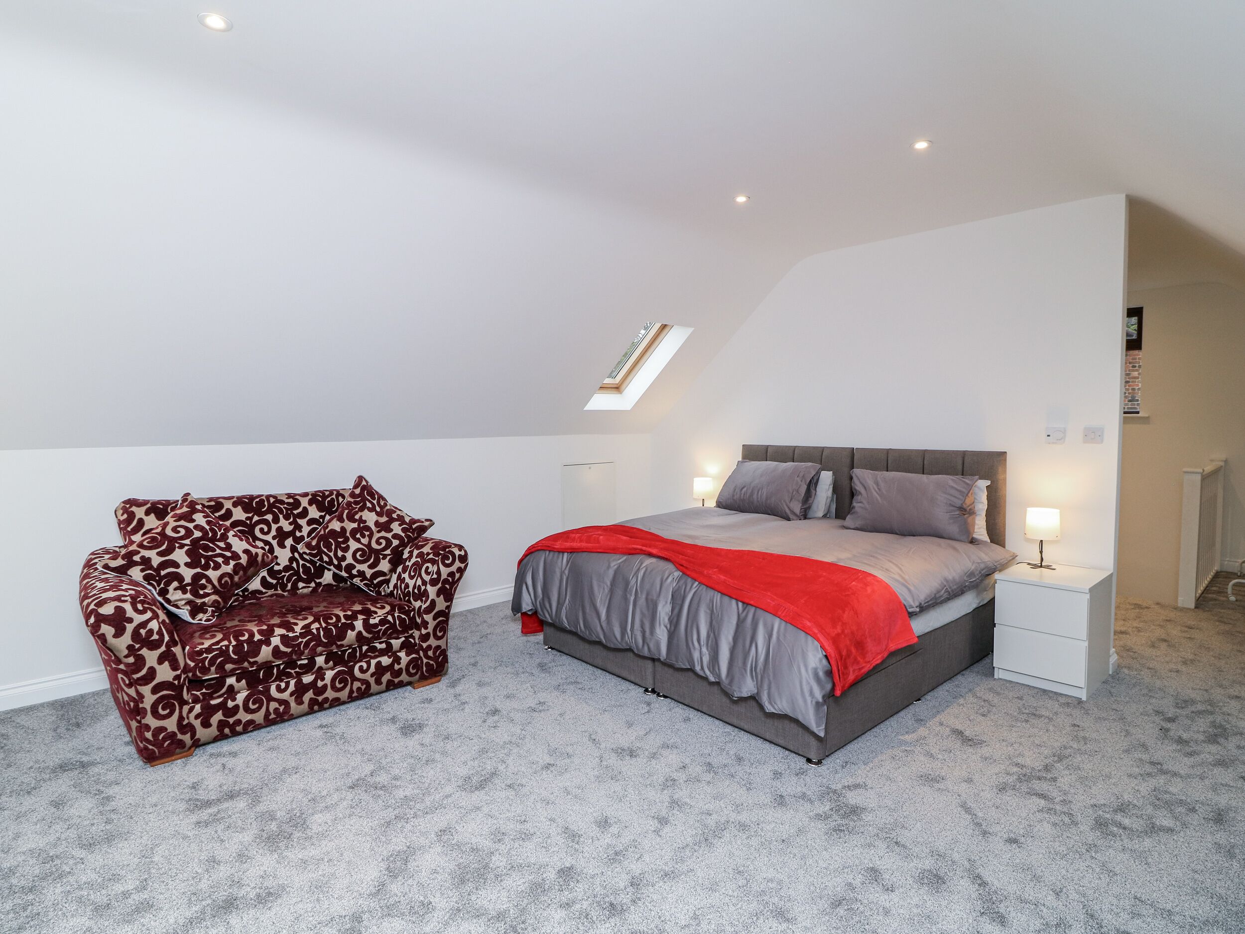 A bedroom with a bed, a patterned sofa, and a skylight.